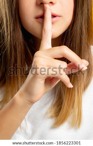Child secret. Hush gesture. Keep quiet. Stop talking. Cropped closeup portrait of brunette teen girl showing shhh with finger at mouth.