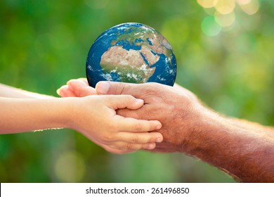 Child and senior holding planet in hands against green spring background. Earth day holiday concept. Elements of this image furnished by NASA