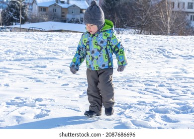 A child with a serious expression on his face in winter clothes jackets, pants, hat and boots in winter on the white snow on the street and in the park in nature plays winter fun.