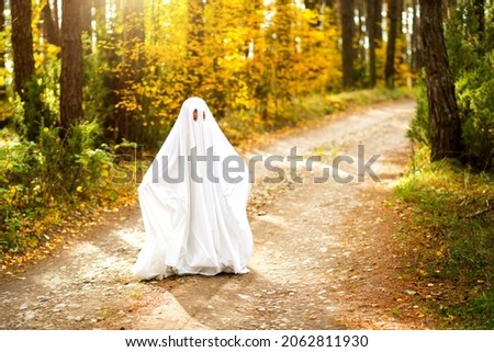 A child in sheets with slits like a ghost costume in an autumn forest scares and terrifies. A kind little ghost. Halloween Party