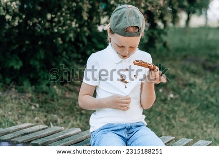 A child showing a chocolate stains on his clothes sitting on a wooden bench in the park. outdoors. The concept of cleaning stains on clothes. High quality photo