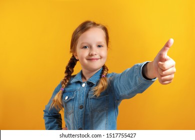 The child shows a thumb up. Little girl in a denim shirt on a yellow background - Shutterstock ID 1517755427