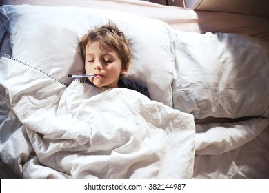 Child Sick In Bed With Fever And Thermometer