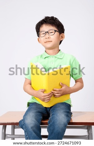 Child sits on a desk while reading a yellow book, showing interest and focus on the content inside