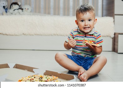 The Child Sits On The Floor And Eats Pizza Very Appetizing And Greedy, In Shorts And A T-shirt