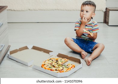 The Child Sits On The Floor And Eats Pizza Very Appetizing And Greedy, In Shorts And A T-shirt