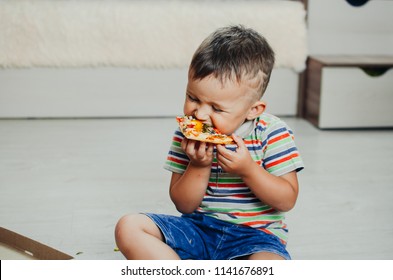 The Child Sits On The Floor And Eats Pizza Very Appetizing And Greedy, In Shorts And A T-shirt