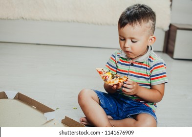 The Child Sits On The Floor And Eats Pizza Very Appetizing And Greedy, In Shorts And A T-shirt