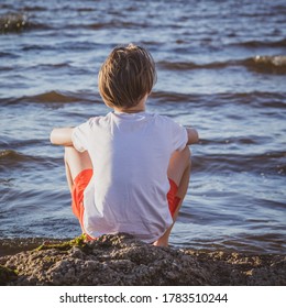 child sits on the seashore, boy looks into the sea at sunset, concept of summer vacation and relaxation