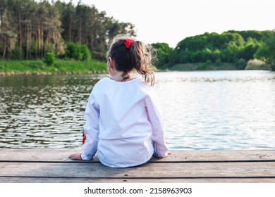 The child sits on a wooden bridge near the river, enjoys the beauty of nature.