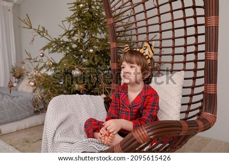 a child sits at rattan chair next to the christmas tree 