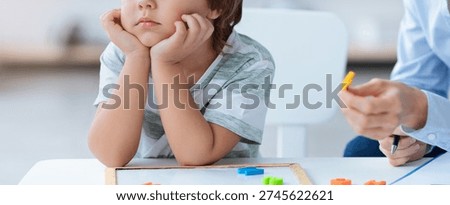 Child Sits at Table With Learning Tools While Adult Engages in Educational Activity