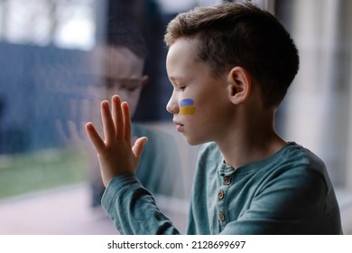 The Child Sits At The Window With The Flag Of Ukraine. State Support In War. United Europe Against Russia. Hope For The World. Anxiety And Anticipation. Children's Tears. Save Ukraine