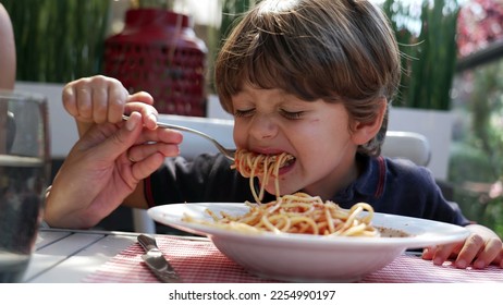 Child sitting at lunch table eating spaghetti. Mother hand feeding pasta to son at restaurant. Noodles with red sauce on plate - Shutterstock ID 2254990197