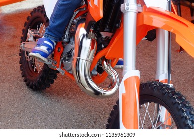 the child is sitting on a small orange sports pitbike, the moto sport theme
