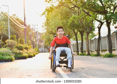 Child Sitting On Wheelchair Is Enjoying Activities In The Park Like Other People. Happy Disabled Kid Concept.