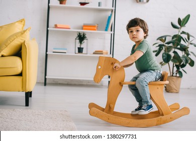 Child Sitting On Wooden Rocking Horse In Living Room