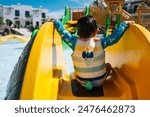 A child is sitting on a yellow slide at a water park. The child 