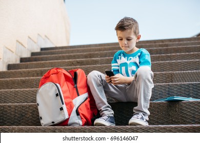 Child Sitting Outside School And Playing Games On His Cell Phone