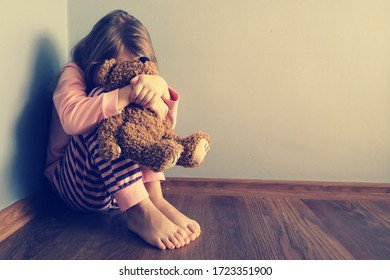 The child is sitting sad scared on the floor in the corner and hugs a toy. Little girl crying with her head down. Concept: No Domestic Violence and Child Abuse. Mistakes of parents in raising children