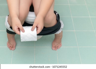 Child Sitting In Toilet And Holding Tissue Roll, Diarrhea Constipation. Health And Cleanliness Concept