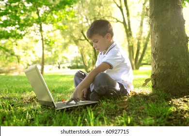 Child Sitting Under A Tree In A Garden And Using A Laptop