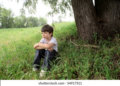 Child Sitting Under A Tree On A Green Meadow