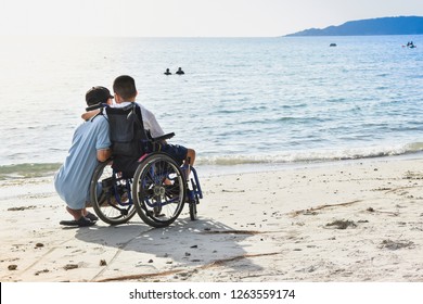 A child sitting in a wheelchair hugging his father's neck at the seaside.