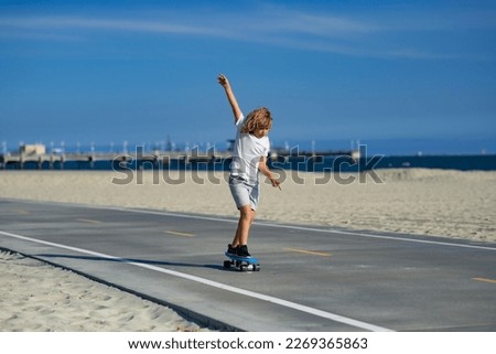 Child skateboarder ride on skateboard in park. Young smiling teenager boy riding on modern cruiser skateboard, urban background. Concept of activity and happy childhood.
