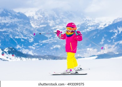 Child Skiing In Mountains. Active Toddler Kid With Safety Helmet, Goggles And Poles. Ski Race For Young Children. Winter Sport For Family. Kids Ski Lesson In Alpine School. Little Skier Racing In Snow