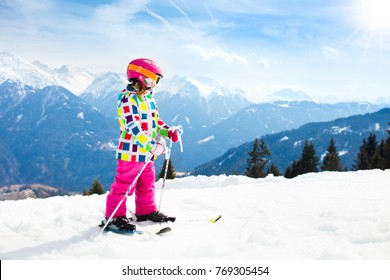 Child Skiing In Mountains. Active Toddler Kid With Safety Helmet, Goggles And Poles. Ski Race For Young Children. Winter Sport For Family. Kids Ski Lesson In Alpine School. Little Skier Racing In Snow