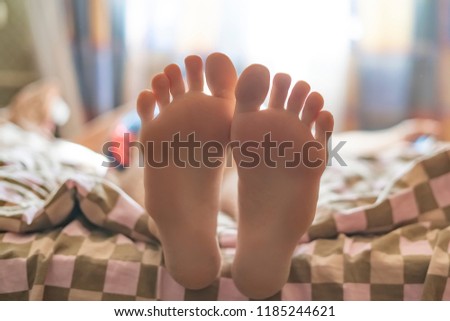 child sleep lying on the bed, close up bare foot in the morning at home against the sunshine throung the window