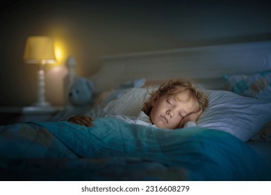 Child sleeping in dark bedroom. Little boy napping. Healthy night rest. Kids room with night light. Toddler with teddy bear. Bedding for children. - Powered by Shutterstock