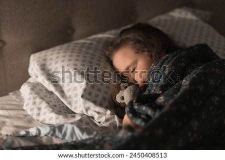 Child sleeping peacefully in bed snuggled up with stuffed monkey, soft lamp light with a pillow and headboard and blankets