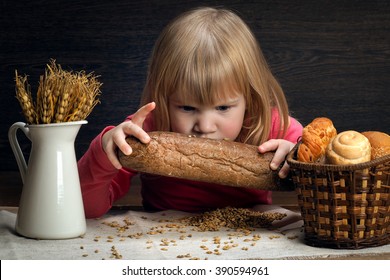 Child Smelling A Loaf Of Rye Pumpernickel. On The Table Grain Oats And Wheat. Ears Of Wheat In The Bread Basket