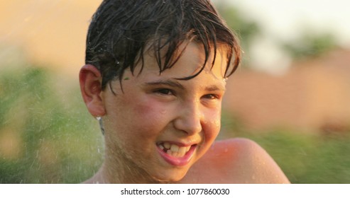 Child smiling to camera while covering ears with hands and water spraying him with sprinkles