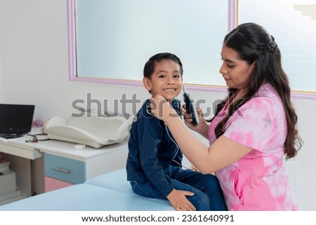 A child smiling at the camera while his pediatrician performs an ear exam or hearing screening