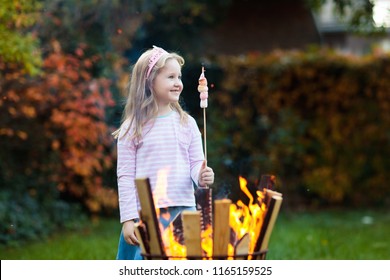 Child With Smores At Camp Fire. Kids Roast Marshmallow On Stick At Bonfire. Autumn Family Outdoor Fun. Camping With Children In Fall Forest. Little Girl Roasting Marshmallows.