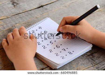 Child solves math examples. Child holds a marker in his hand and writes answers to multiplication examples in notebook. Learning multiplication table concept. Homeschool education.  Kid math studying