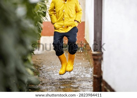 Child splashing through a flooded path in yellow rain boots and a raincoat, enjoying outdoor play during wet weather after heavy rain.