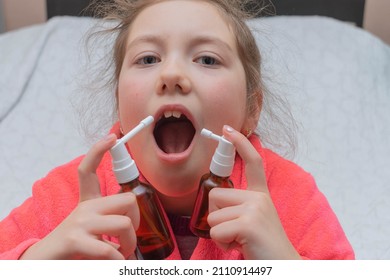 The Child Sprays The Medicine Into His Mouth With Two Aerosols. The Girl Is Trying To Cure Her Sore Throat. Portrait Of A Child Taking Medication For A Sore Throat.