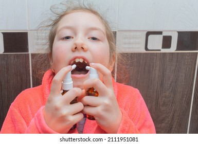 The Child Sprays The Medicine Into His Mouth With Two Aerosols. The Girl Is Trying To Cure Her Sore Throat. Portrait Of A Child Taking Medication For A Sore Throat.