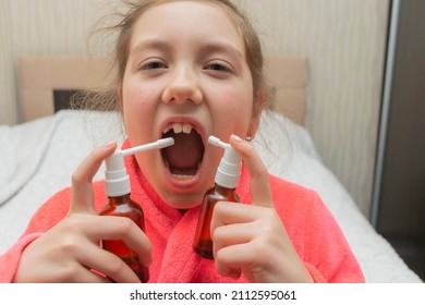 The Child Sprays The Medicine Into His Mouth With Two Aerosols. The Girl Is Trying To Cure Her Sore Throat. Portrait Of A Child Taking Medication For A Sore Throat.