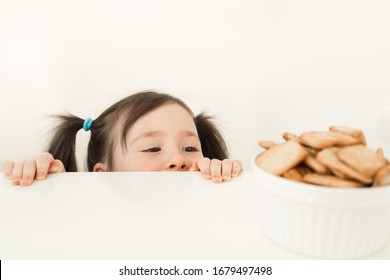 A Child Spying On Cookies. Baby Wants To Steal Sweets. Girl Peeks Out From The Table