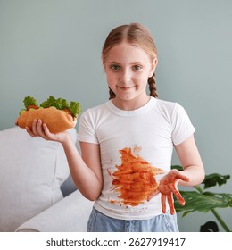 El niño se manchó la ropa con ketchup. Una chica come un perrito caliente.