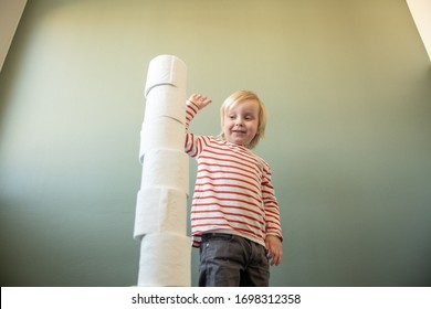 Child Standing Against A Green Wall Playing And Stacking And Building Towers With Toilet Paper Rolls