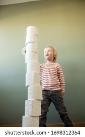 Child Standing Against A Green Wall Playing And Stacking And Building Towers With Toilet Paper Rolls