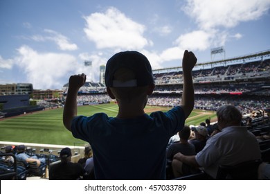 Child Standing And Cheering At A Baseball Game. Silhouette View From Behind
