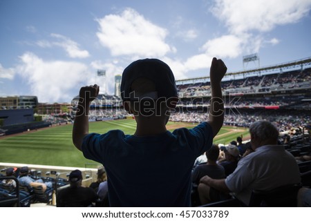 Child standing and cheering at a baseball game. Silhouette view from behind