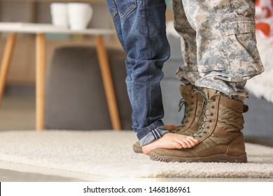 Child standing of feet of his military father at home